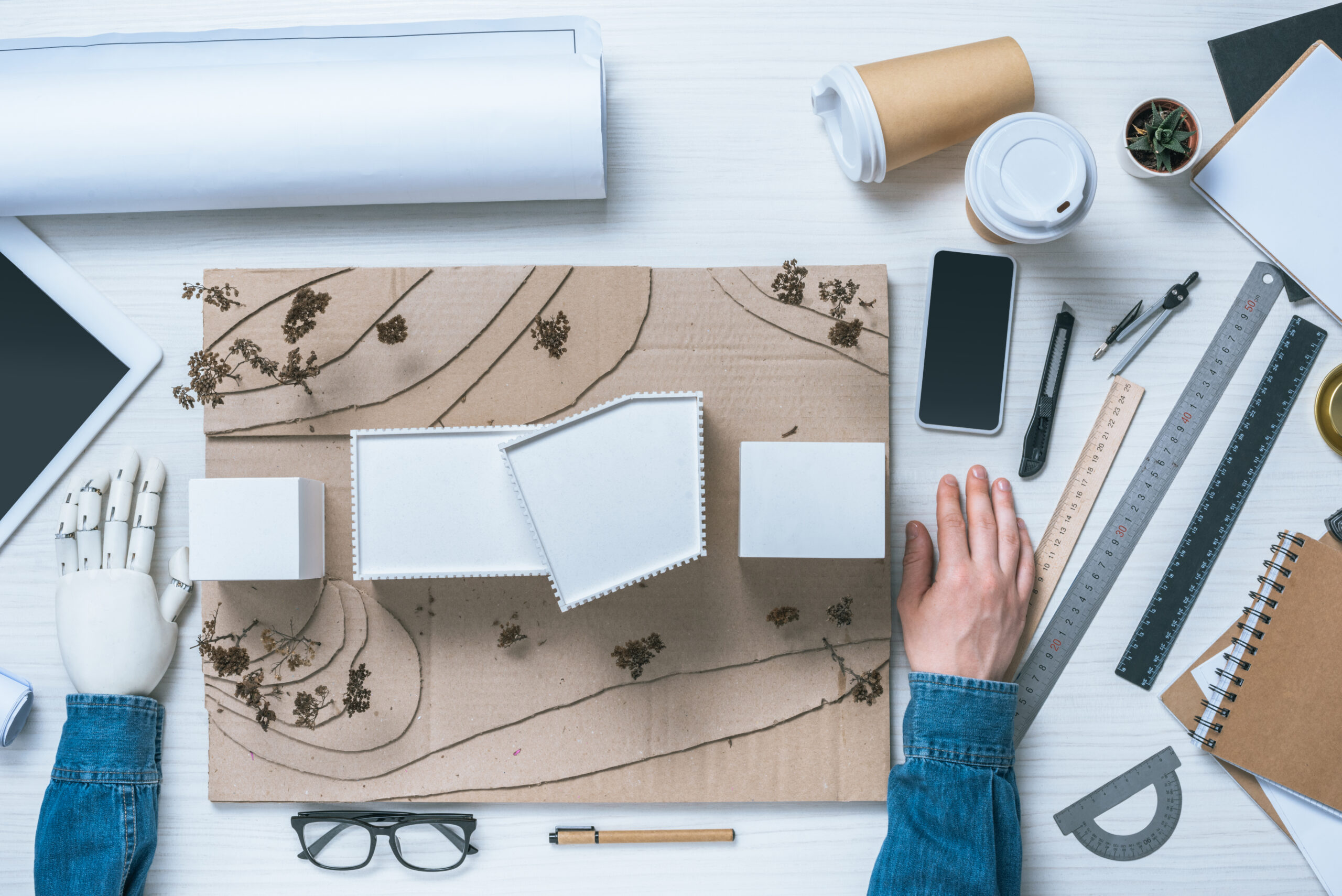cropped image of male architect with prosthetic arm sitting at table with model of house, rulers,
