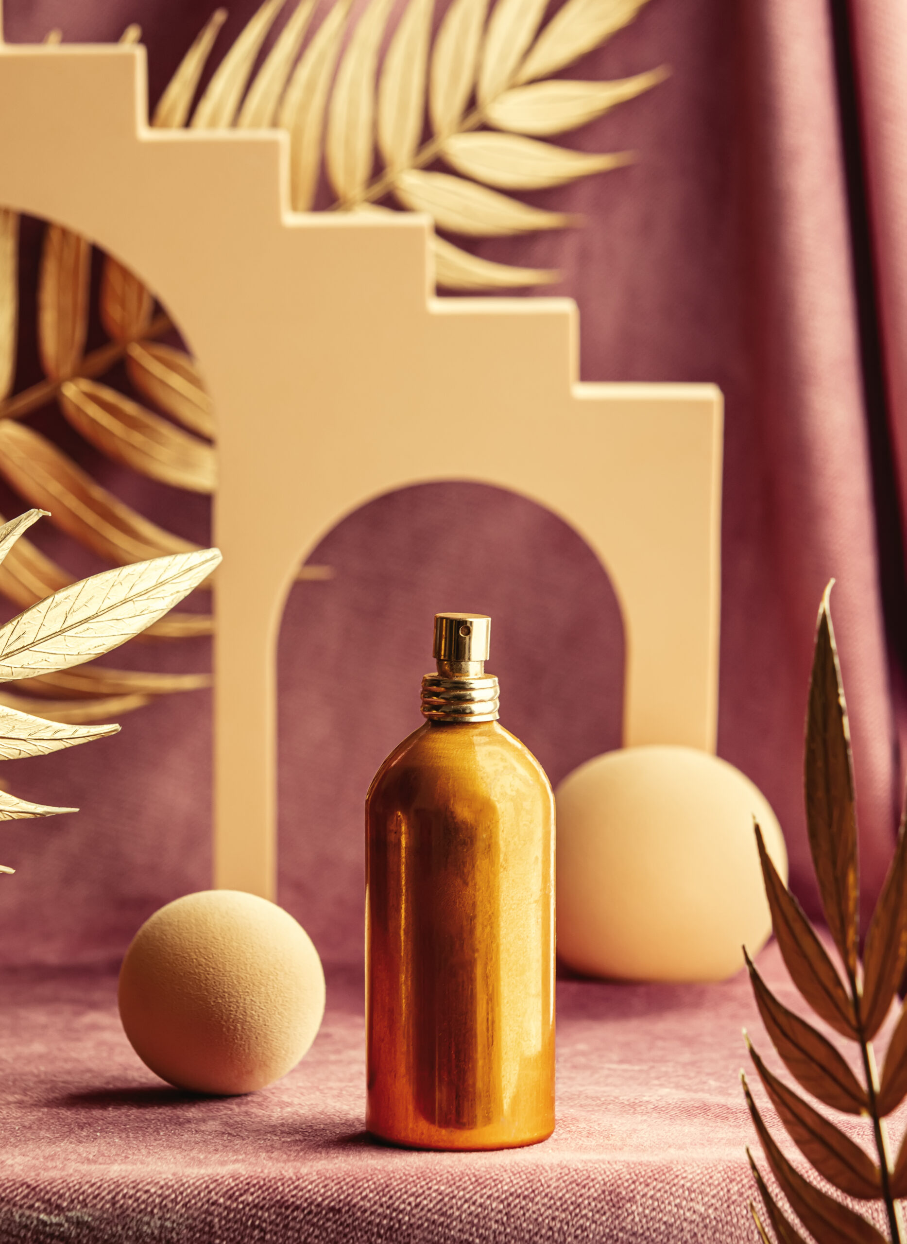 presentation of golden perfume bottle next to geometric shapes and palm leaves