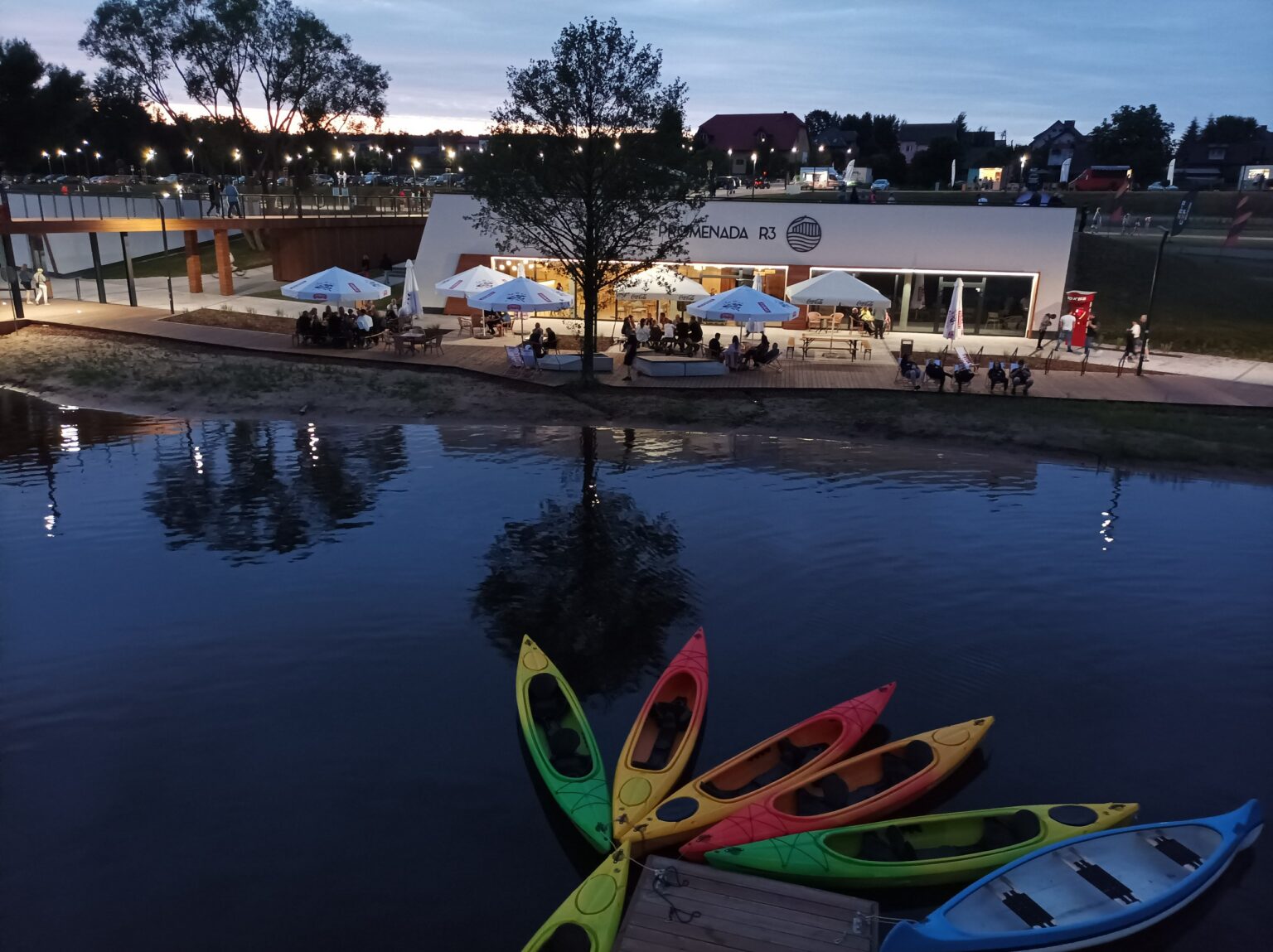 Kolorowe kajaki i oświetlony pawilon nad zalewem Lubianka wieczorem; wizytówka Google dla firm ze Starachowic