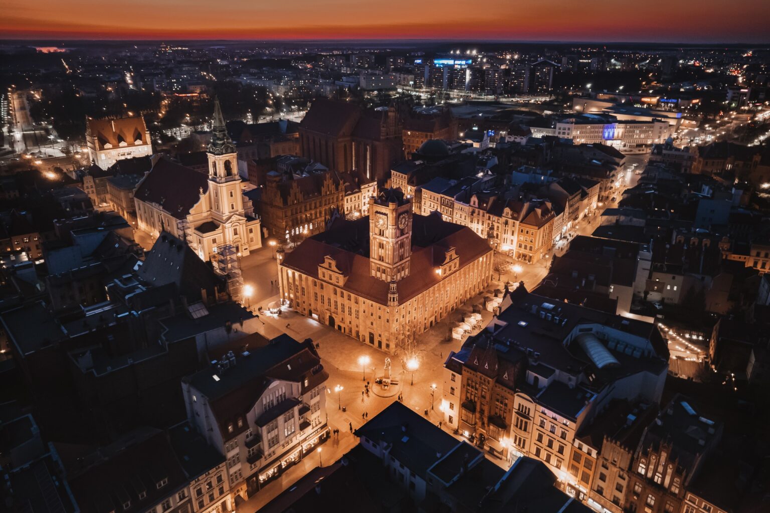 Oświetlony Ratusz Staromiejski i rynek w Toruniu o zmierzchu; strony internetowe dla firm z Torunia