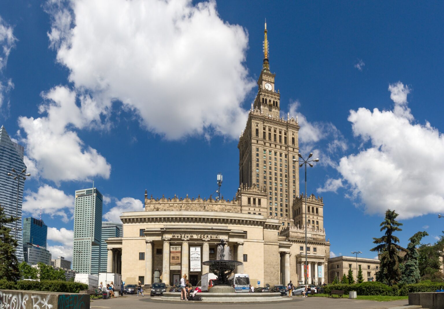 Pałac Kultury i Nauki na tle błękitnego nieba z chmurami, wieżowce Warszawy w tle; pozycjonowanie stron dla firm z Warszawy