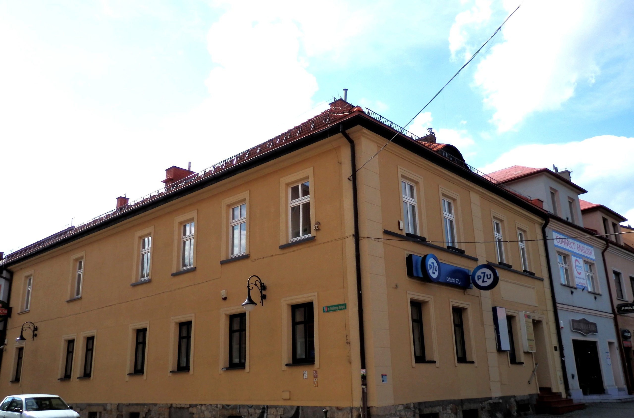 Narożna kamienica w centrum Żor z oddziałem PZU i szkołą językową, pusta ulica w słońcu; wizytówka Google dla firm z Żor