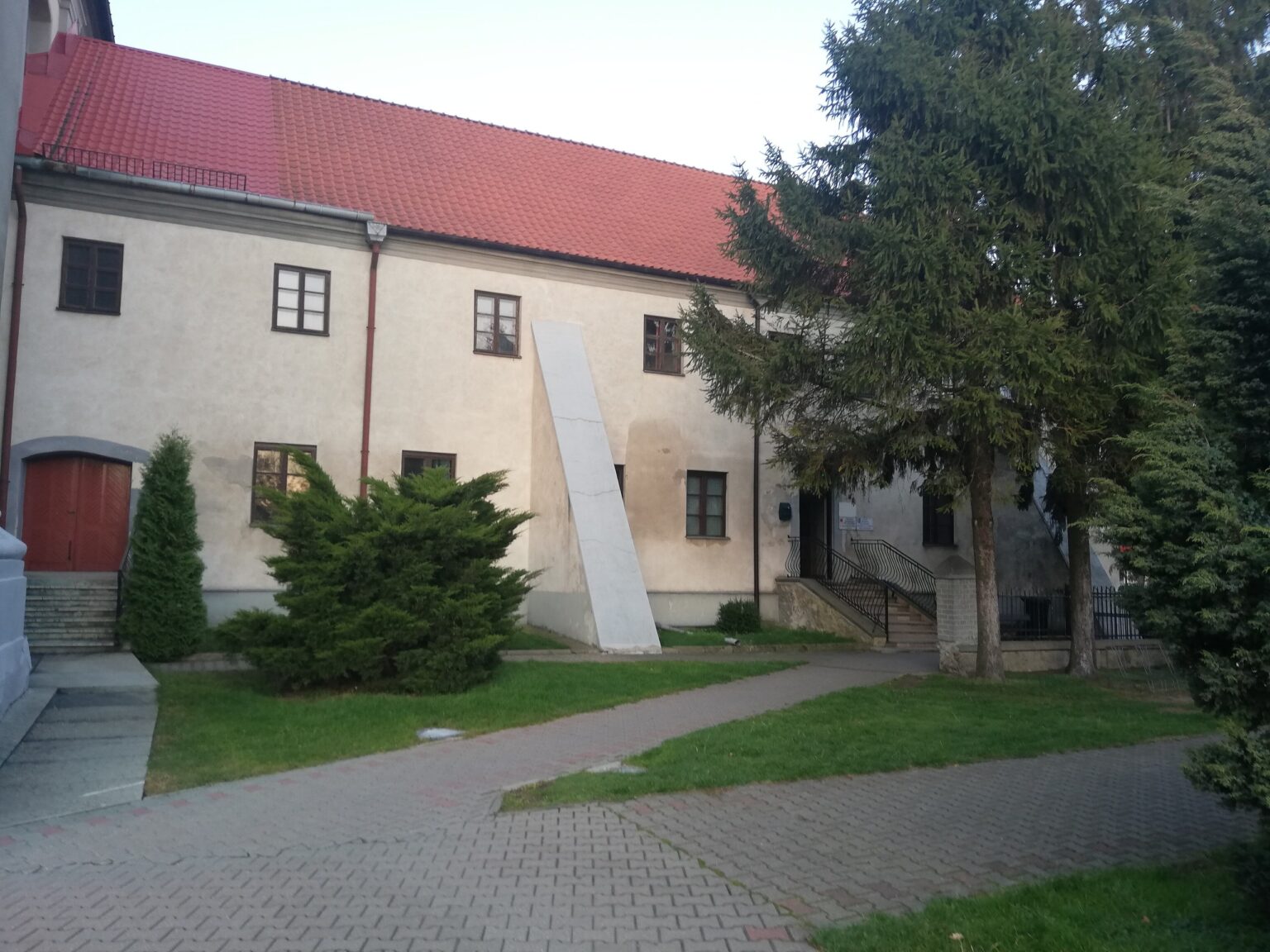 Zabudowania pobenedyktyńskiego zespołu poklasztornego w Żurominie, biały budynek z czerwonym dachem i tujami; pozycjonowanie stron internetowych dla firm z Żuromina
